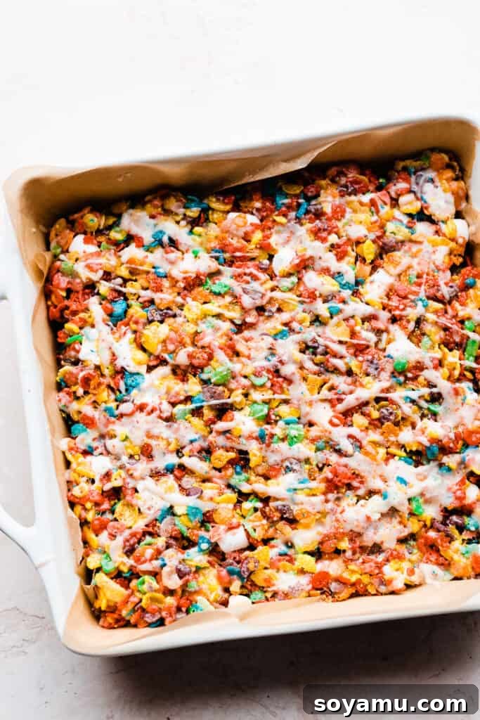 A pan of colorful Fruity Pebbles treats generously topped with a sweet cereal glaze and crushed cereal bits.