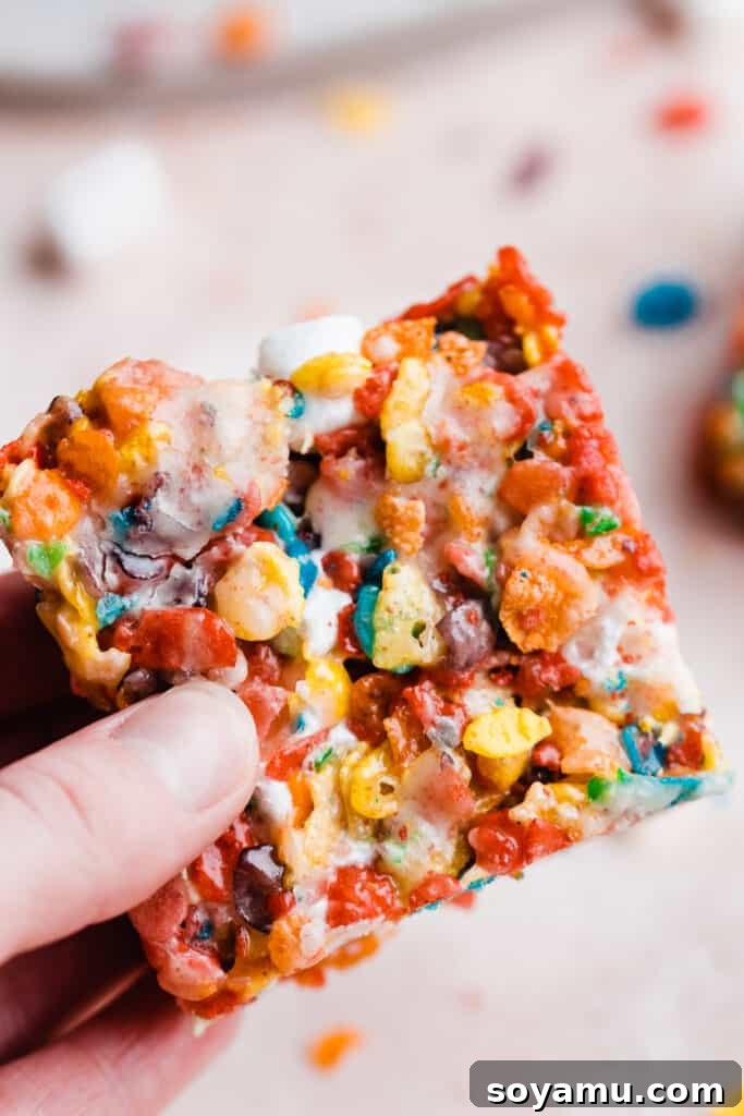 A hand holding up a single, perfectly crafted brown butter Fruity Pebbles treat, showing its colorful layers and soft interior.