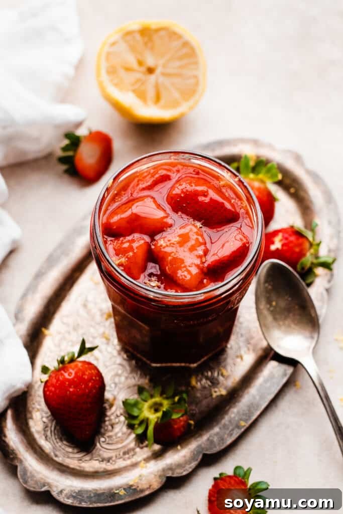 Easy 10-Minute Strawberry Compote 2 A jar of freshly made strawberry compote on a rustic vintage metal tray, showcasing its vibrant red color and natural texture.
