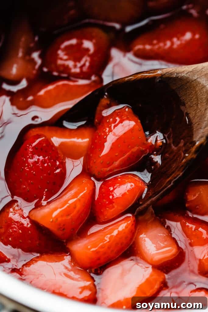 Easy 10-Minute Strawberry Compote 6 A close-up shot of a wooden spoon stirring rich strawberry compote in a glass jar, showing its glossy texture and whole berry pieces.