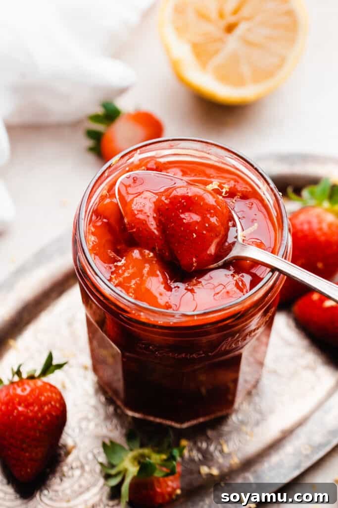 Easy 10-Minute Strawberry Compote 8 A spoon dipping into a jar of glistening strawberry sauce, served on a vintage metal tray, ready for use.