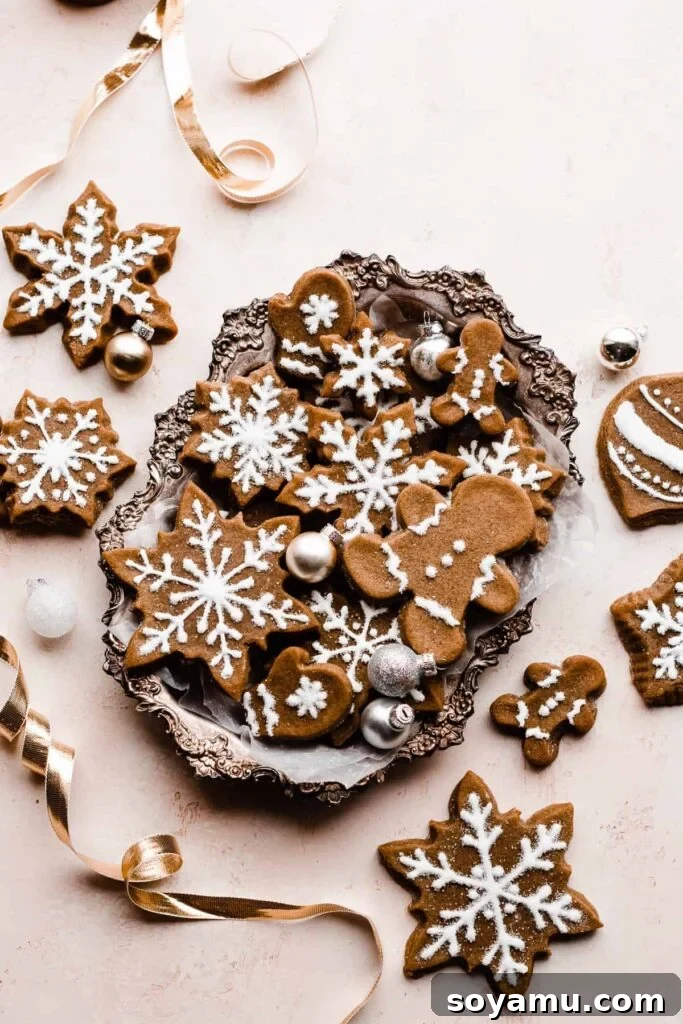 A platter of beautifully iced gingerbread cookies, adorned with mini ornaments and gold ribbon, showcasing a festive holiday spread.