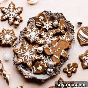 Gingerbread cookies piped with royal icing, arranged in a silver tray and surrounded by festive gold ribbon and mini ornaments.