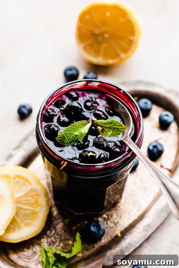 A jar of freshly made blueberry sauce with a spoon digging in, showcasing its thick, rich texture.