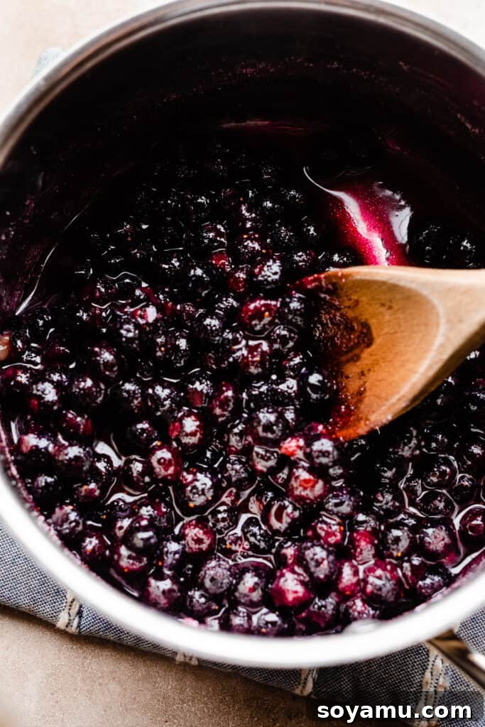 A pot of blueberry sauce gently cooking on the stove, with berries releasing their juices.