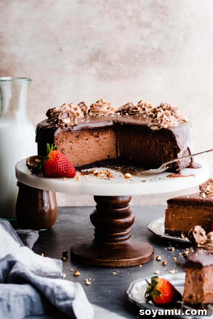 The sliced cheesecake on a stand with individual slices on plates, topped with ganache and whipped cream.