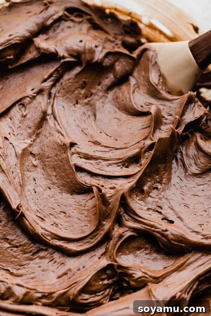 A close-up shot of rich, dark chocolate fudge frosting swirled in a bowl, showcasing its silky smooth texture.