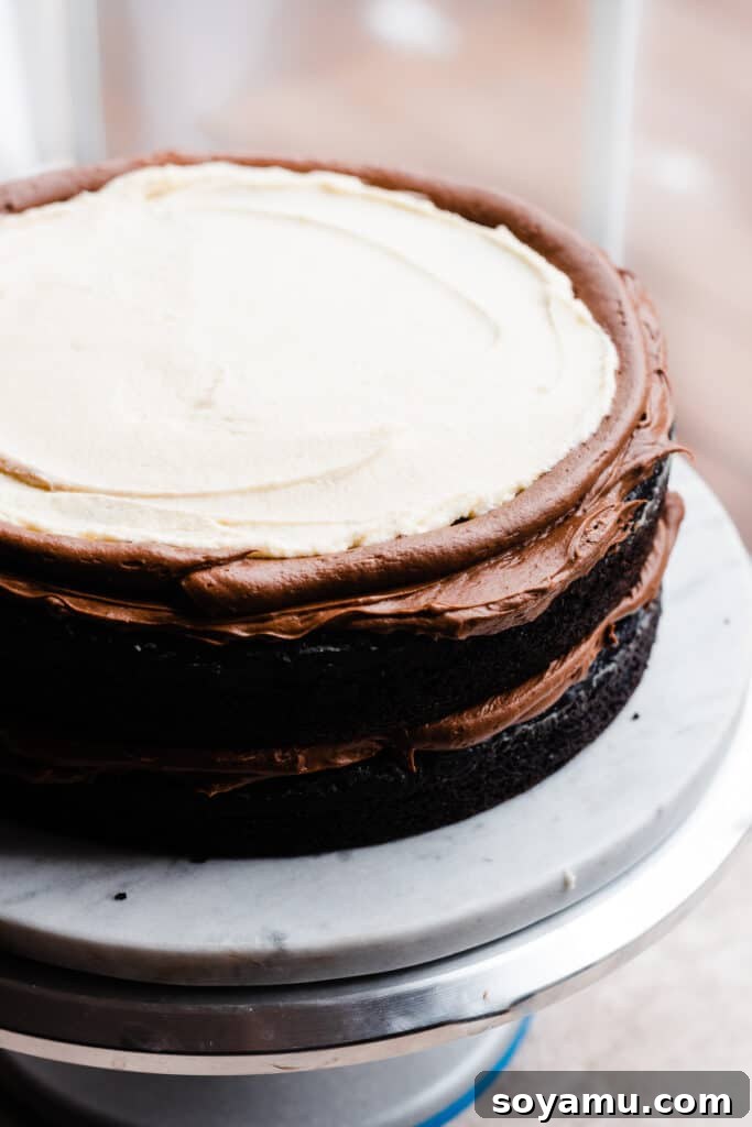 A multi-layered Tuxedo Cake being assembled on a turntable, with distinct layers of chocolate cake and white ganache becoming visible.