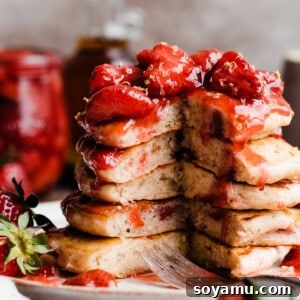 Fluffy Strawberry Pancakes with Speedy Strawberry Compote 12 A stack of strawberry pancakes with a section missing, topped in strawberry compote.