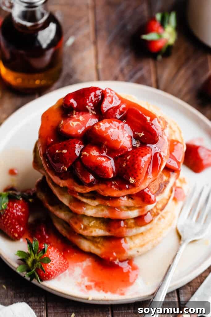 Fluffy Strawberry Pancakes with Speedy Strawberry Compote 3 A top-down view of a stack of golden strawberry pancakes, lavishly topped with shimmering homemade strawberry compote and a pat of melting butter.