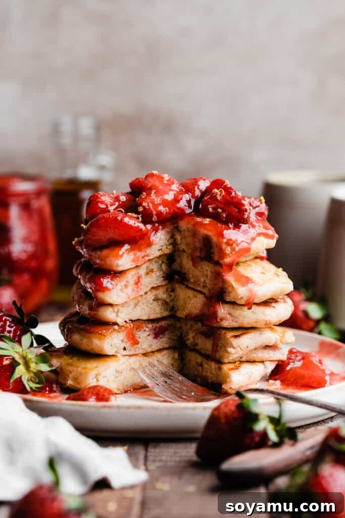 Fluffy Strawberry Pancakes with Speedy Strawberry Compote 9 A beautifully stacked tower of strawberry pancakes, generously topped with glistening strawberry compote and a dusting of powdered sugar.