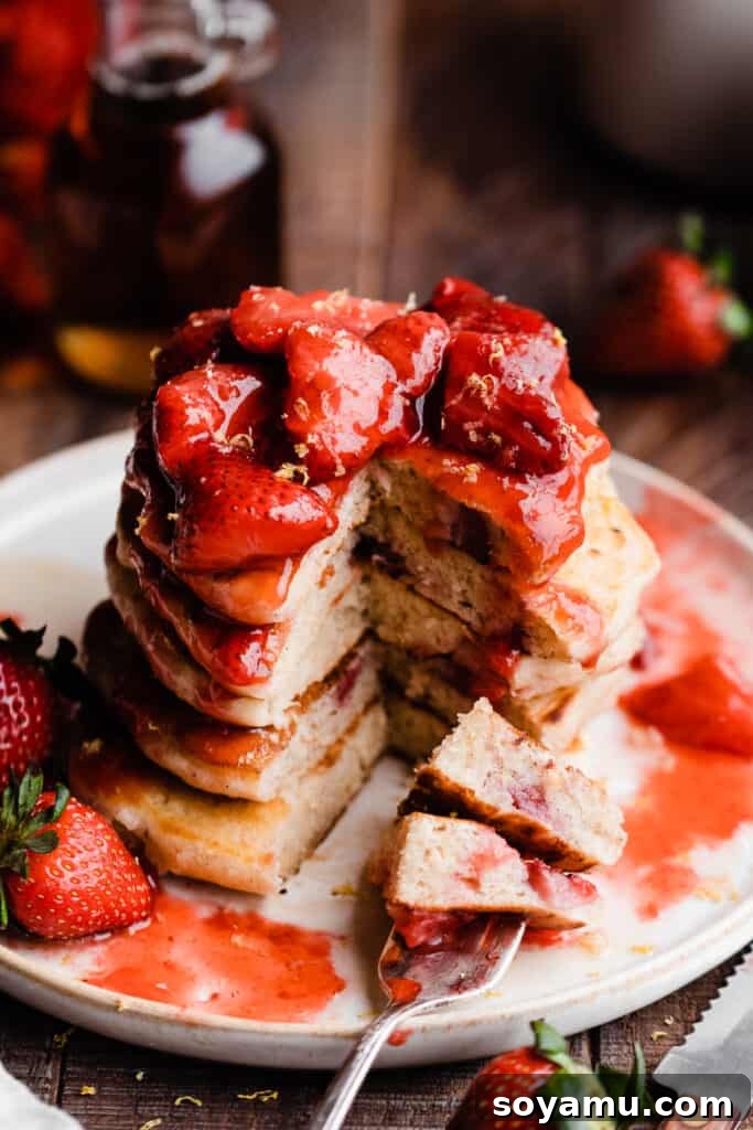 Fluffy Strawberry Pancakes with Speedy Strawberry Compote 10 A 3/4 angle view of a generous stack of strawberry pancakes, glistening with compote and ready to be served.