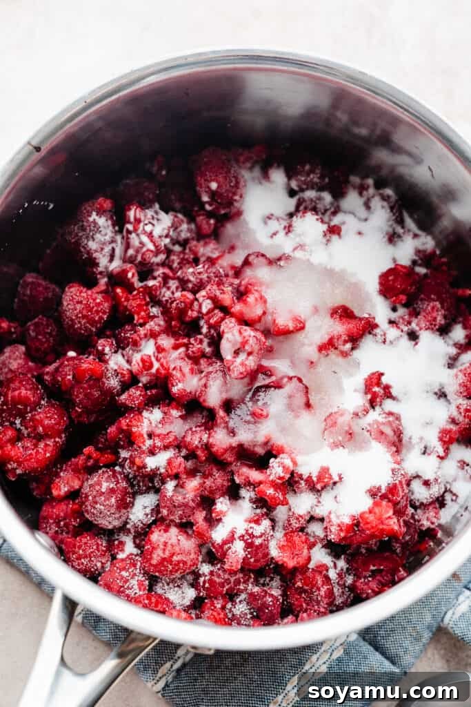 Fresh raspberries, sugar, lemon juice, and cornstarch slurry being added to a saucepan.