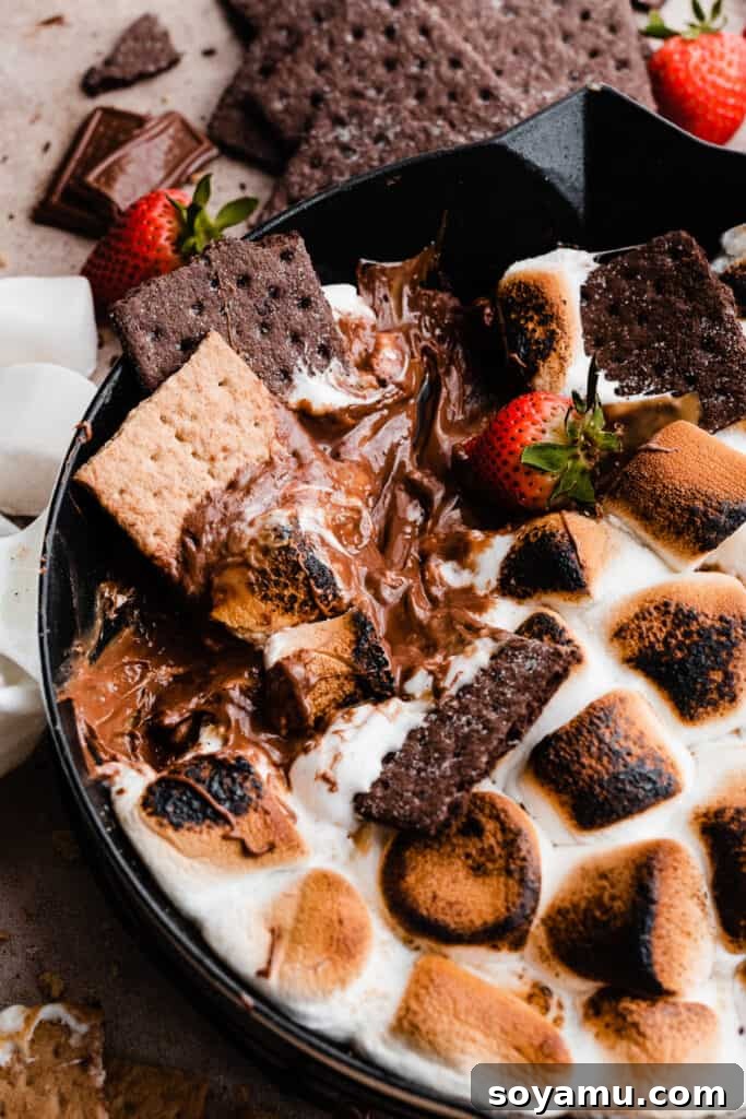 Simple 15 Minute Skillet Smores Dip 9 An inviting overhead shot of the Skillet S'mores Dip being scooped by graham crackers, clearly showing the rich, melted interior and the perfectly toasted marshmallow topping.