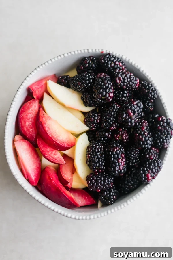 A rustic bowl filled with fresh, vibrant apples, juicy plums, and plump blackberries, ready for baking.
