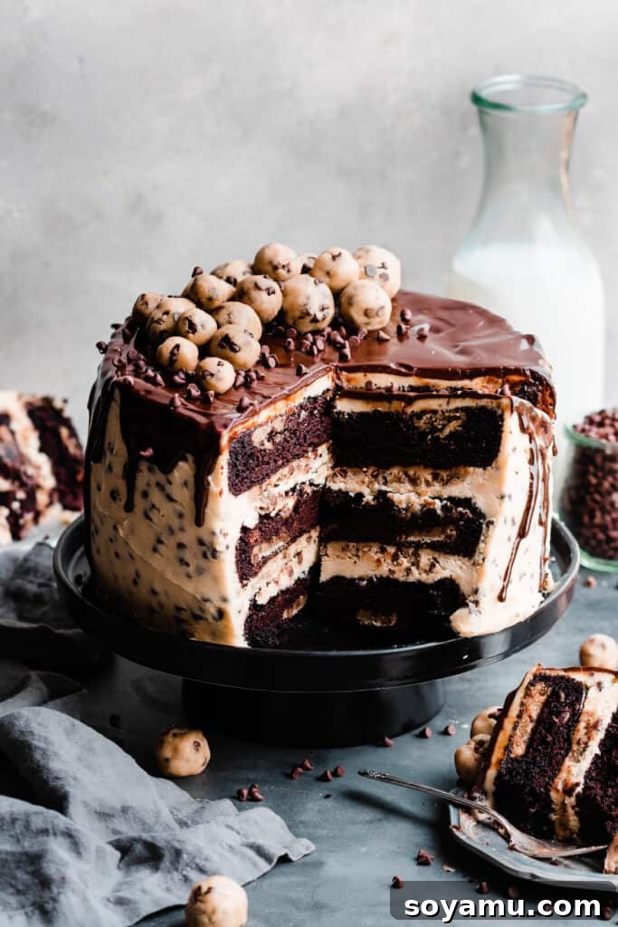 Decadent Cookie Dough Cake 10 The sliced open cookie dough cake on a cake stand, topped with ganache and cookie dough balls, with a bottle of milk in back.