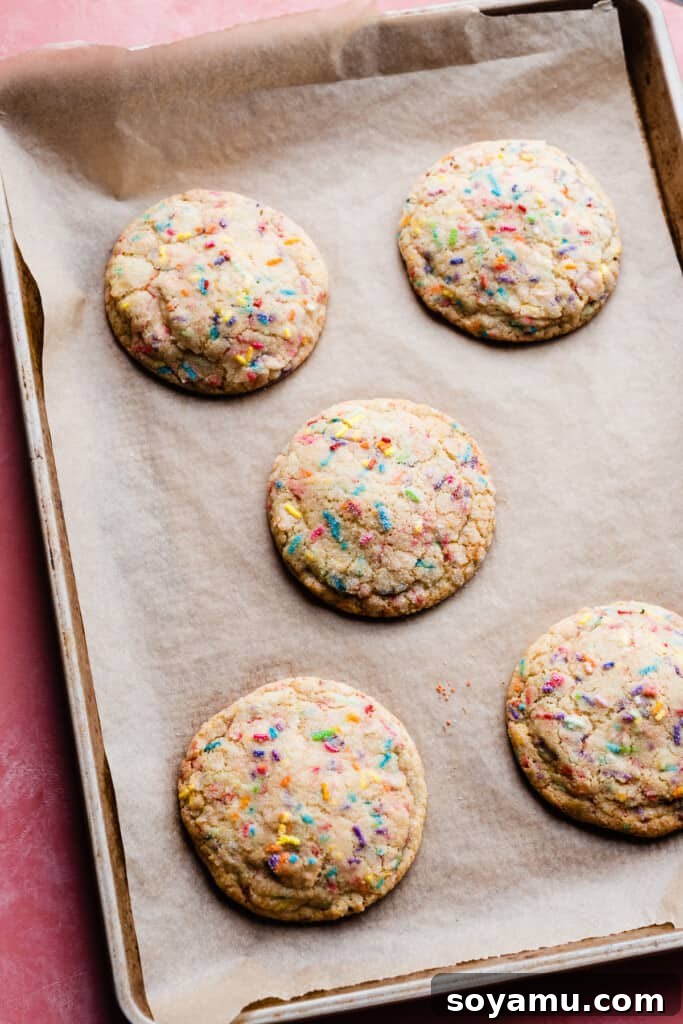 Irresistible Funfetti Cookies with a Cake Batter Cheesecake Surprise 8 A fresh batch of golden, baked funfetti cookies adorned with colorful sprinkles, cooling on a parchment-lined baking sheet, emanating a delightful aroma.