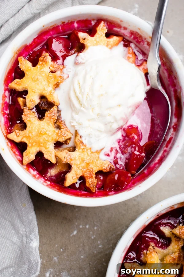 Two individual cherry cobblers baked in ramekins, topped with pie crust snowflakes.