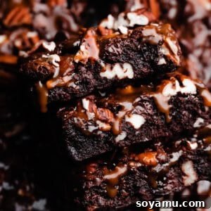 A close-up on a stack of turtle brownies with salted caramel sauce dripping down the sides.