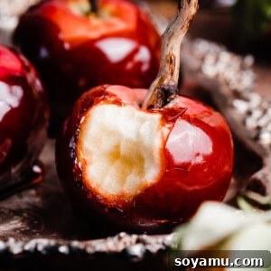 A close-up of a candy apple with a bite missing, highlighting its shiny, hard coating and the crisp apple within, presented on a vintage tray.