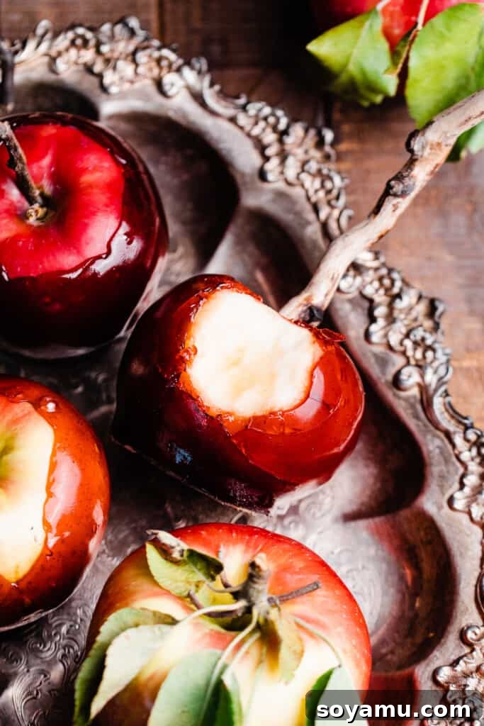 A close-up of a homemade candy apple with a bite missing, displaying its perfectly hard and glossy red coating, resting on a vintage tray.