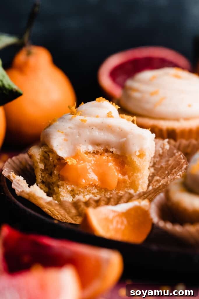 A vibrant plate of orange cupcakes, with one cupcake beautifully halved to reveal its creamy orange curd filling, all topped with a generous swirl of orange cream cheese frosting.