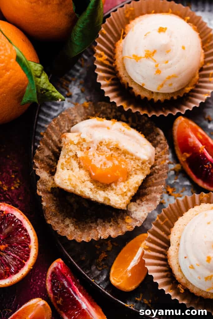 A captivating close-up of half an orange cupcake resting on a white plate, showcasing its soft interior, visible orange curd filling, and fluffy frosting.