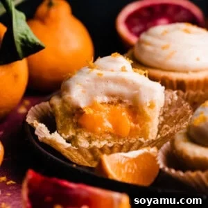 A mouth-watering orange cupcake on a plate, with a section removed to showcase the irresistible orange curd filling.