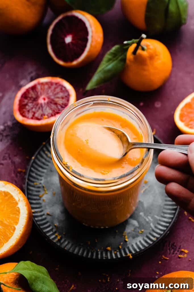 A spoon delicately scooping into a jar filled with homemade, vibrant orange curd, highlighting its smooth and thick texture.