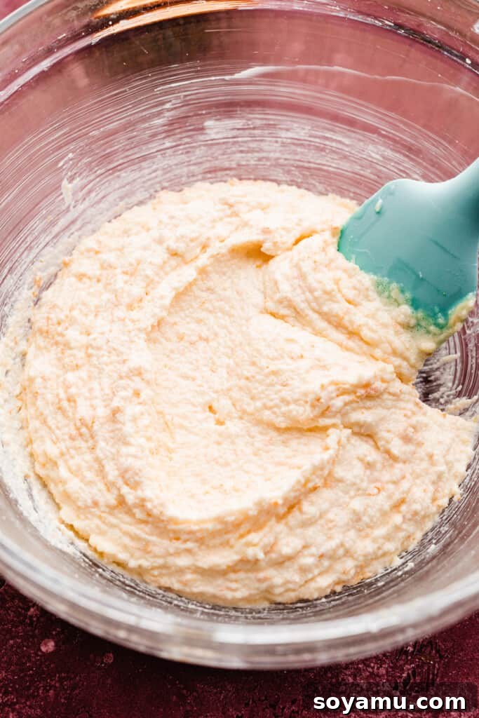 A mixing bowl containing the perfectly creamed butter, vegetable oil, granulated sugar, and orange zest mixture, appearing light and fluffy.