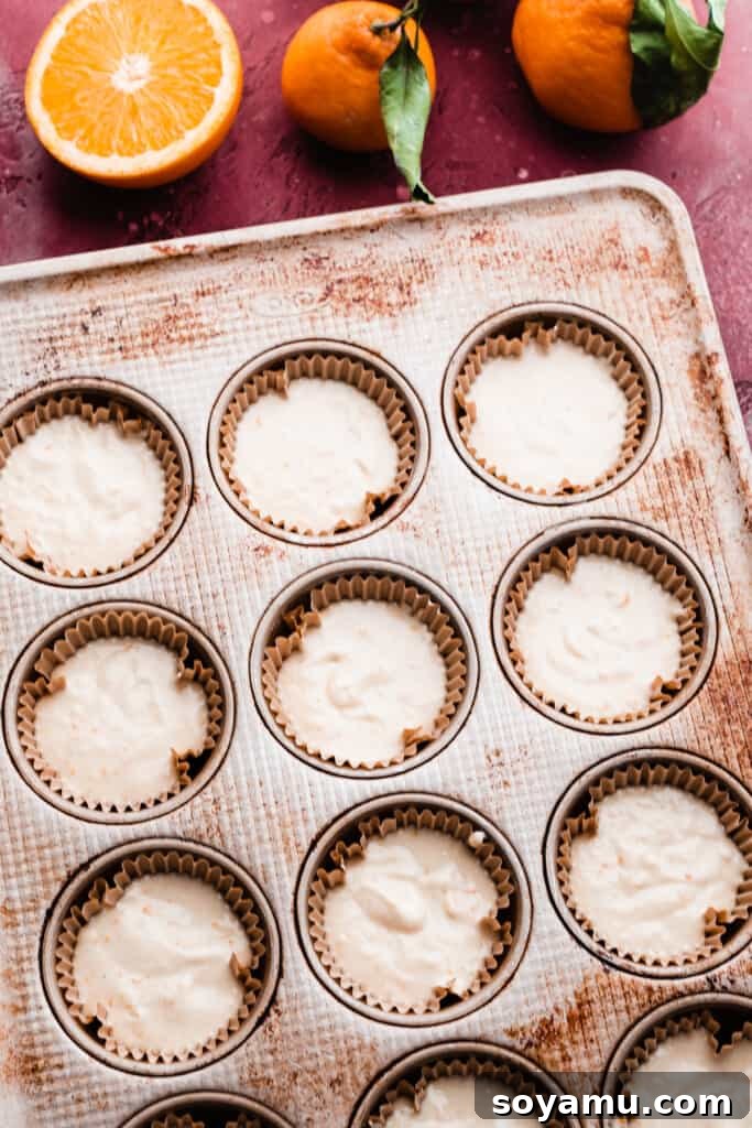 A muffin tin filled with cupcake liners, each generously holding the smooth, unbaked orange cupcake batter, ready to go into the oven.