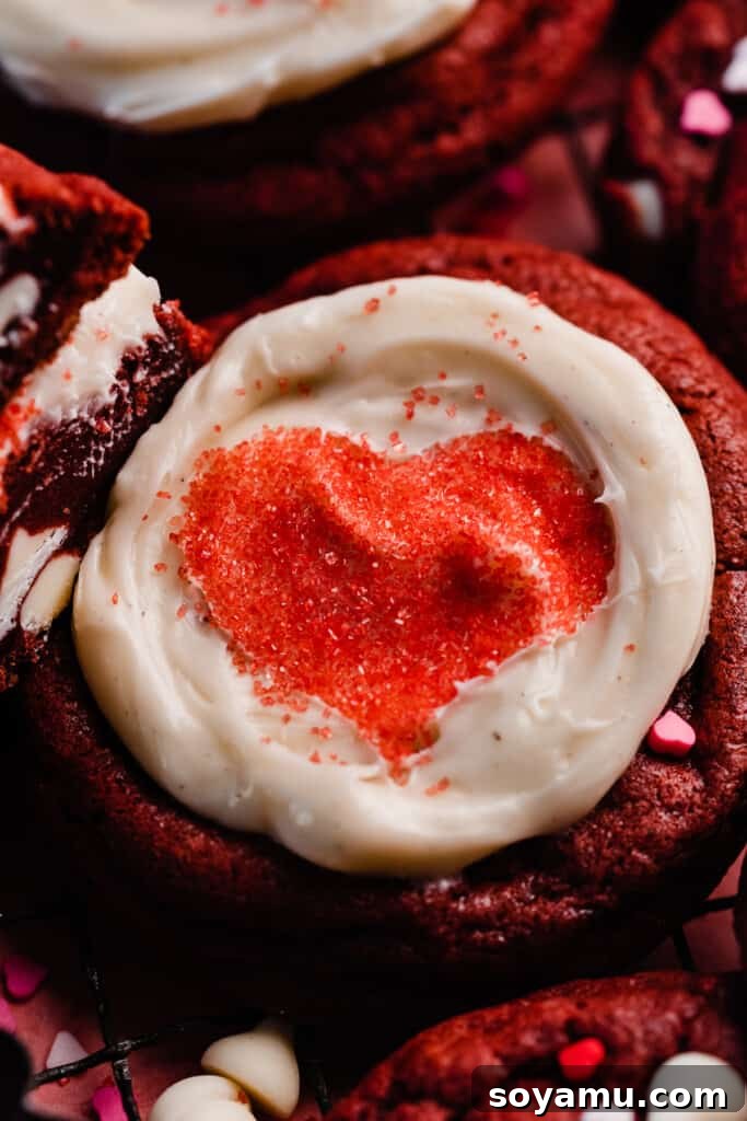 Decadent Red Velvet Cookies with Cream Cheese Frosting 11 A beautifully frosted red velvet cookie, topped with smooth cream cheese frosting and a perfectly defined red heart made from sprinkles, in a close-up shot that highlights the elegant decoration.