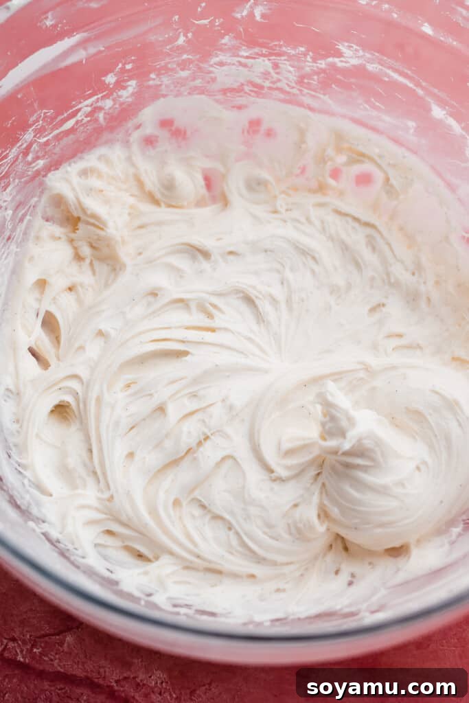 Decadent Red Velvet Cookies with Cream Cheese Frosting 7 A close-up shot of a bowl filled with fluffy, white cream cheese frosting, perfectly whipped and ready to be spread onto the red velvet cookies.