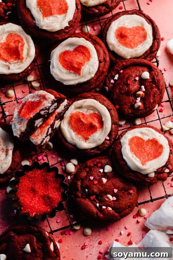 Decadent Red Velvet Cookies with Cream Cheese Frosting 10 A wide-angle shot of numerous perfectly baked and frosted red velvet cookies, elegantly displayed on a vintage wire cooling rack against a soft pink background, creating a charming and inviting scene.