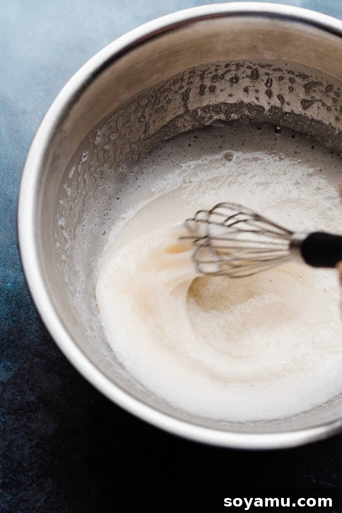A metal mixing bowl containing the cooked egg white and sugar mixture, which forms the base for the Swiss meringue, looking smooth and ready for whipping.