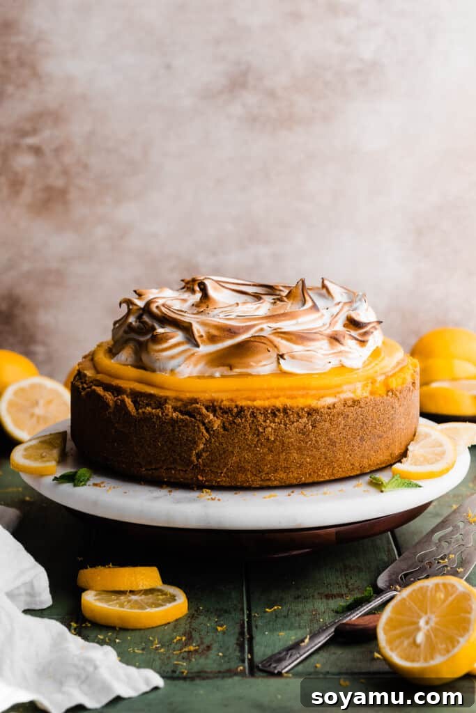 The impressive, fully assembled Lemon Meringue Cheesecake standing tall on a marble cake stand, ready to be sliced and enjoyed.