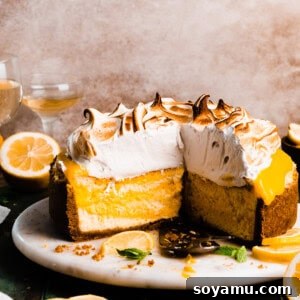 The sliced open lemon meringue cheesecake on a cake stand, showing the layers of crust, lemon cheesecake, lemon curd, and meringue topping.