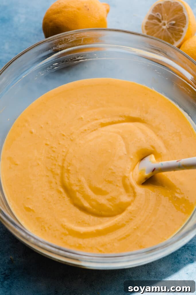 A close-up view of a bowl containing the vibrant lemon curd cheesecake batter, visibly smoother and richer after the addition of the curd.