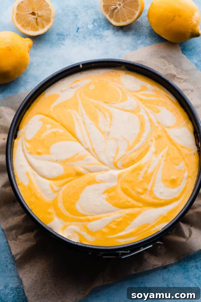 The unbaked lemon meringue cheesecake in a springform pan, showcasing the elegant swirls of two different lemon batters before going into the oven.
