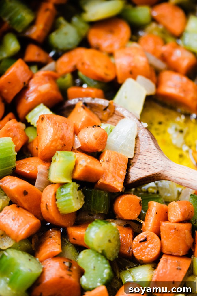 Soulful Chicken Wild Rice Soup 4 A close-up of a spoon stirring the aromatic medley of carrots, celery, and onion as they soften in a pan, releasing their savory fragrance.