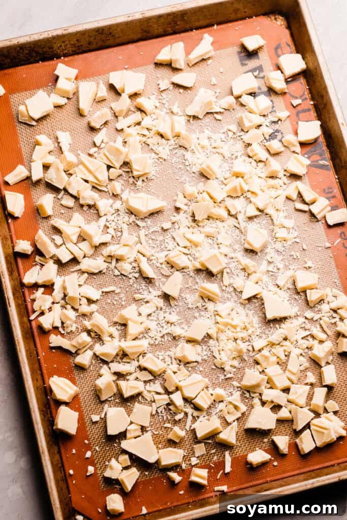 Unlocking the Flavor of Caramelized White Chocolate 4 Roughly chopped pieces of white chocolate spread in a single, even layer on a silicone-lined baking sheet, ready for the oven.