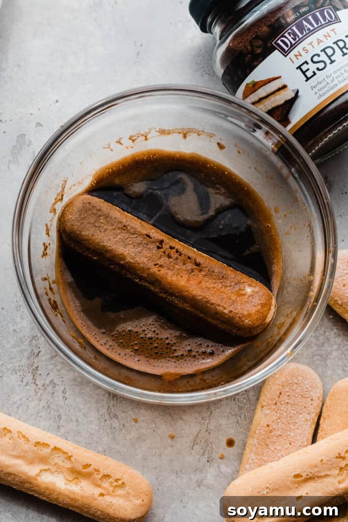 Decadent Mocha Tiramisu Cheesecake 6 A ladyfinger being quickly dipped into a bowl of rich, dark espresso.