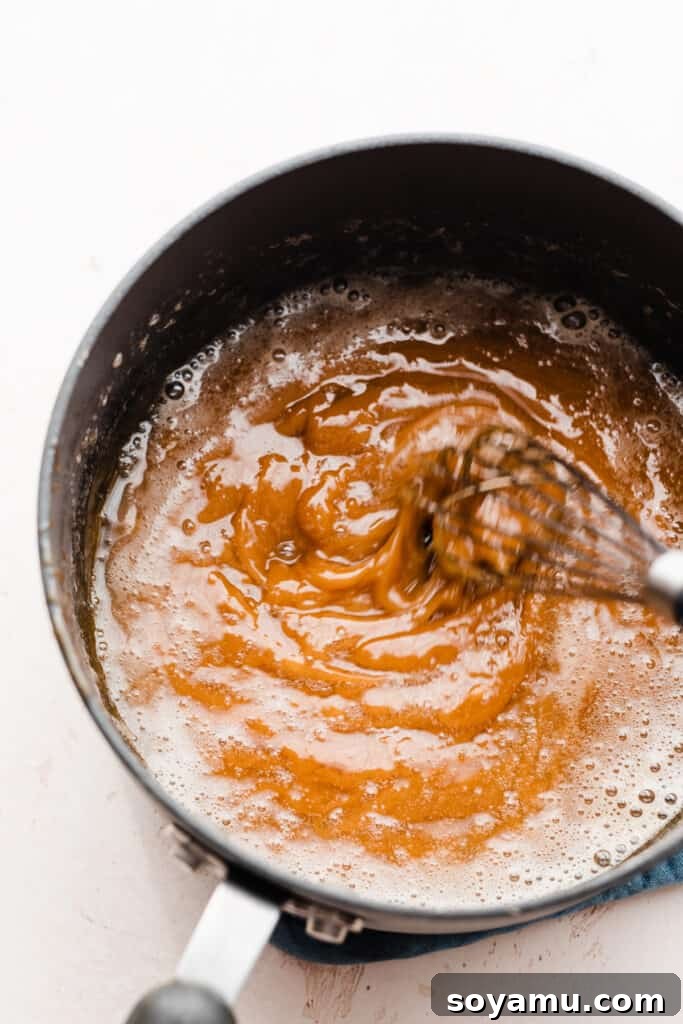 Decadent 10-Minute Salted Caramel Sauce 5 A whisk blending cubed butter into the molten, amber-colored sugar, creating a rich base.