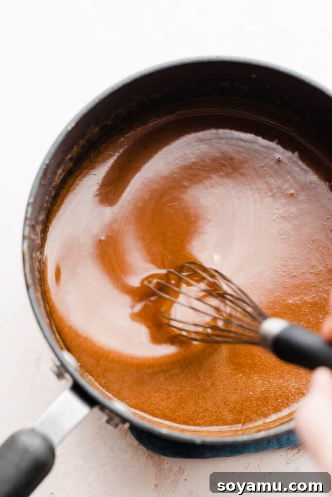 Decadent 10-Minute Salted Caramel Sauce 6 A whisk stirring the caramel sauce after adding heavy cream, showing a slightly clumpy but still smooth consistency.