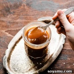 A spoon dipping into a jar of rich, golden salted caramel sauce.