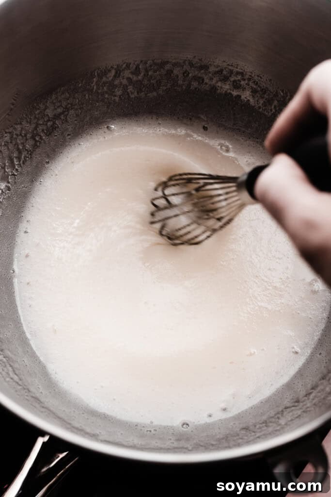 Crafting Silky Smooth Swiss Meringue 6 A hand whisking the egg white and sugar mixture gently over a simmering water bath, demonstrating the cooking process.