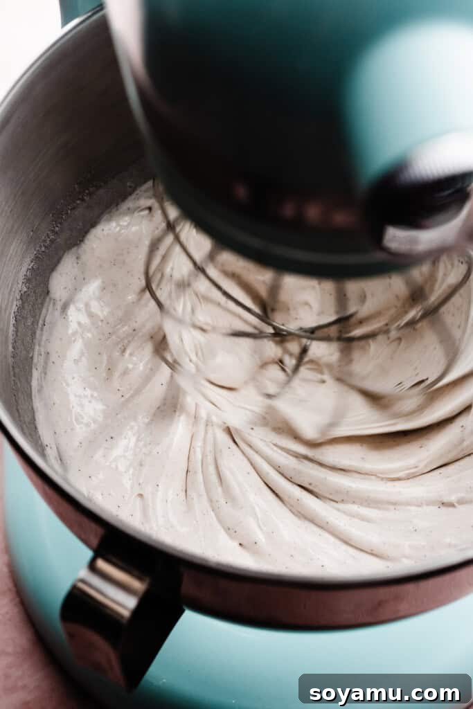 Crafting Silky Smooth Swiss Meringue 7 The Swiss meringue mixture beginning to gain volume and thicken, being whipped vigorously by a stand mixer's whisk attachment.