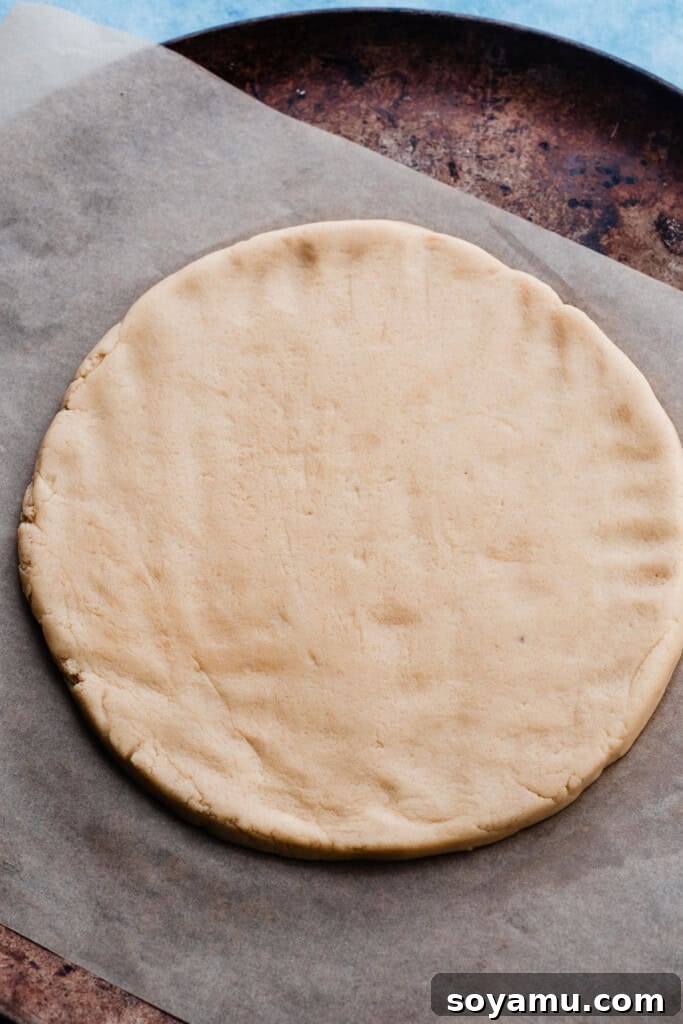 The unbaked sugar cookie dough, neatly pressed into a round shape on parchment paper, chilling on a baking sheet, preparing for its transformation into a perfect fruit pizza crust.