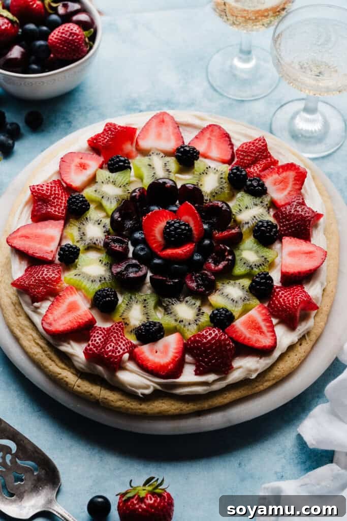 The fully decorated Fruit Pizza, adorned with a vibrant assortment of fresh berries and kiwi, artfully arranged on a large platter, inviting guests to enjoy a slice.