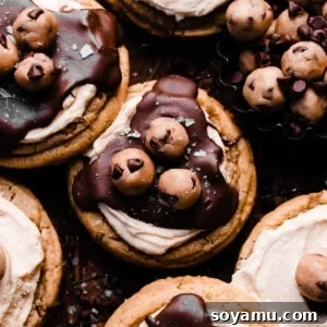 Chocolate covered cookie dough cookies topped with edible cookie dough bites on a dark backdrop.